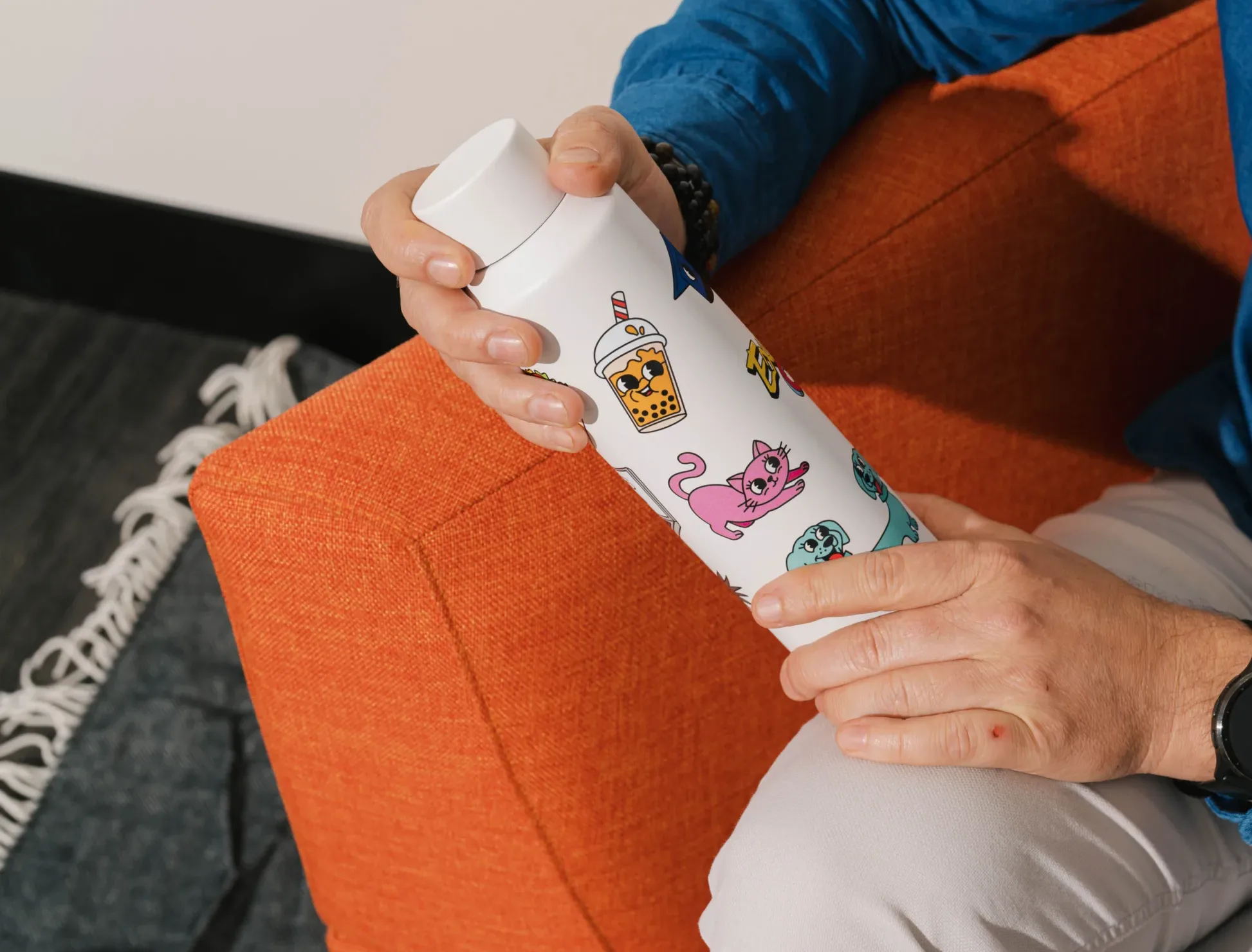 A white water bottle with colorful cartoon stickers held by a person.