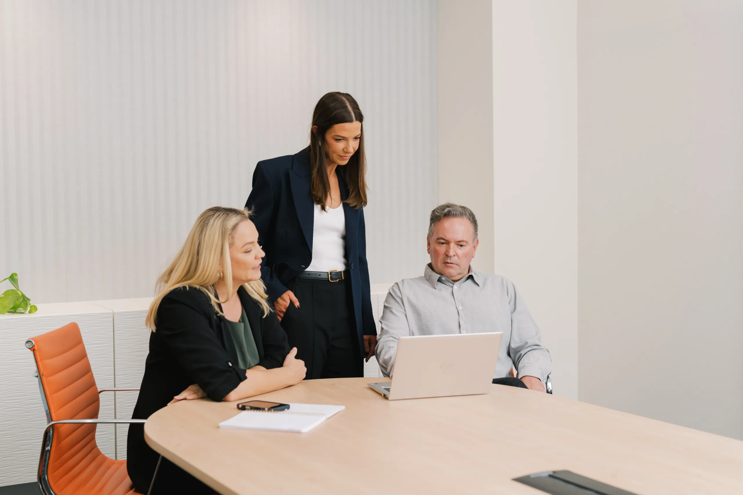 Three professionals in a meeting room looking at a laptop.